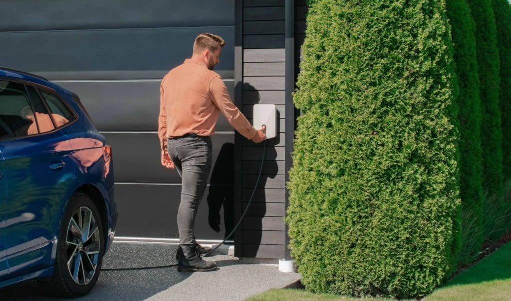 Man walking to garage to plug electric vehicle into evnex ev charger