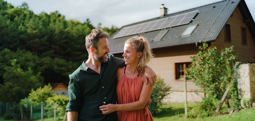 Happy couple standying near their house with a solar panels. Alternative energy, saving resources and sustainable lifestyle concept.