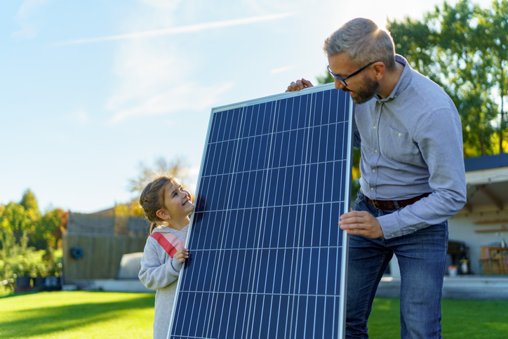 Father with his little daughter near the house with solar panels. Alternative energy, saving resources and sustainable lifestyle concept.