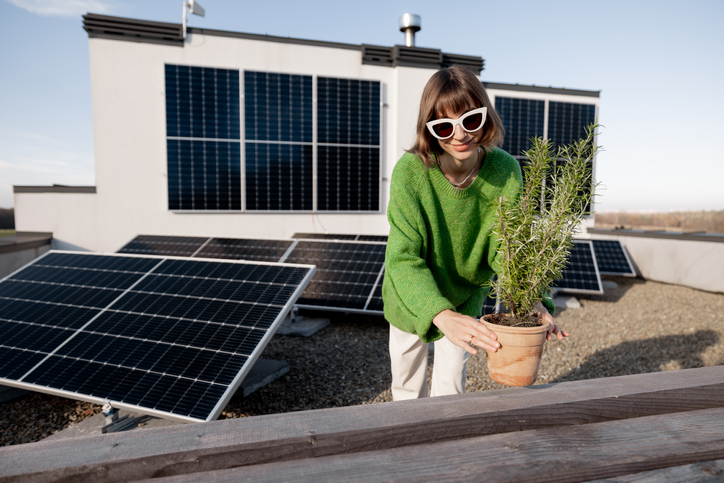 Portrait of a happy woman stands with green plant on a rooftop with a solar power plant installed on it. Alternative energy, eco-friendly and sustainable lifestyle