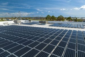Aerial view of blue photovoltaic solar panels mounted on industrial building roof for producing clean ecological electricity. Production of renewable energy concept.